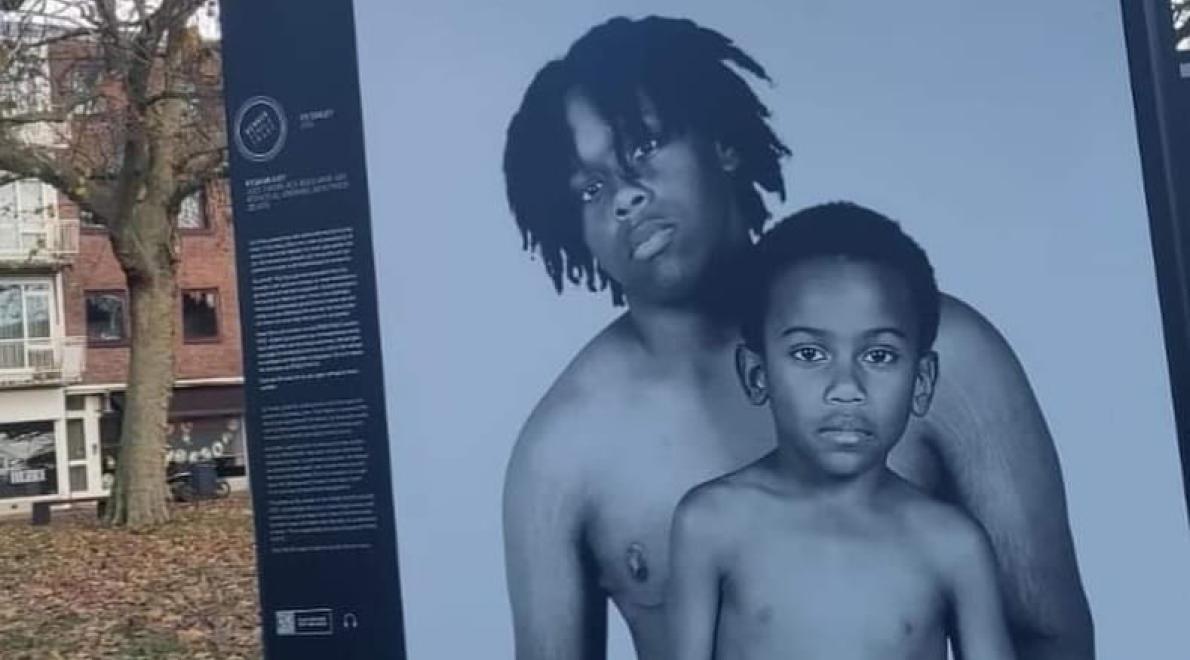 Foto uit de pride photo exhibition waarop een zwarte jongetransman en zijn zesjarige broertje met ontblote bovenlijven te zien zijn.