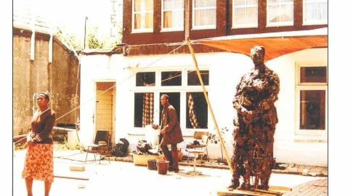 Nelson Carrilho werkend aan het beeld Mama Baranka in zijn tijdelijke studio in de Valkenburgerstraat, zomer 1984. Zijn moeder staat model. Foto: collectie Nelson Carrilho